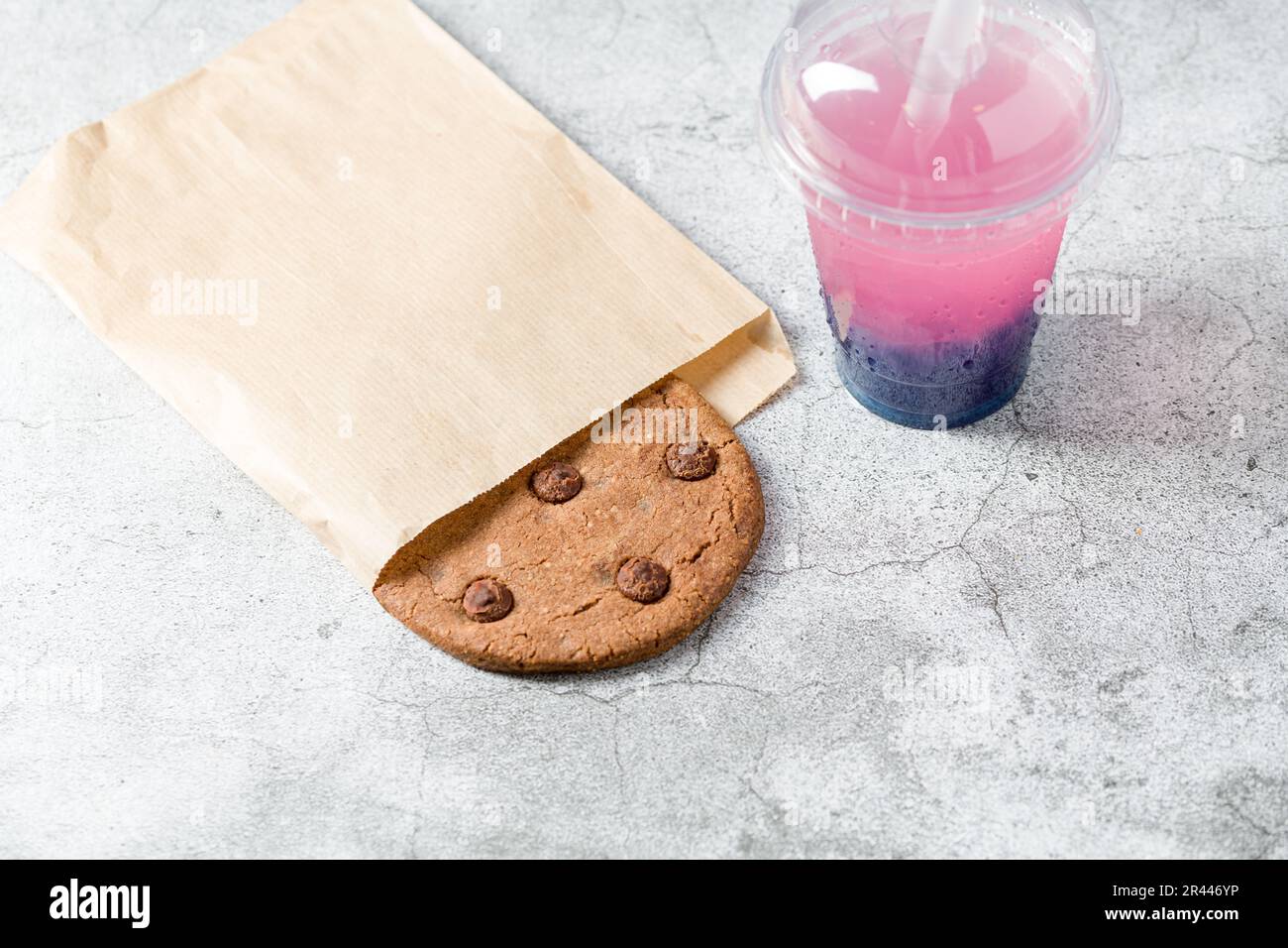 Biscuit aux pépites de chocolat emballé dans un sac en papier avec une boisson à côté sur une table en pierre Banque D'Images