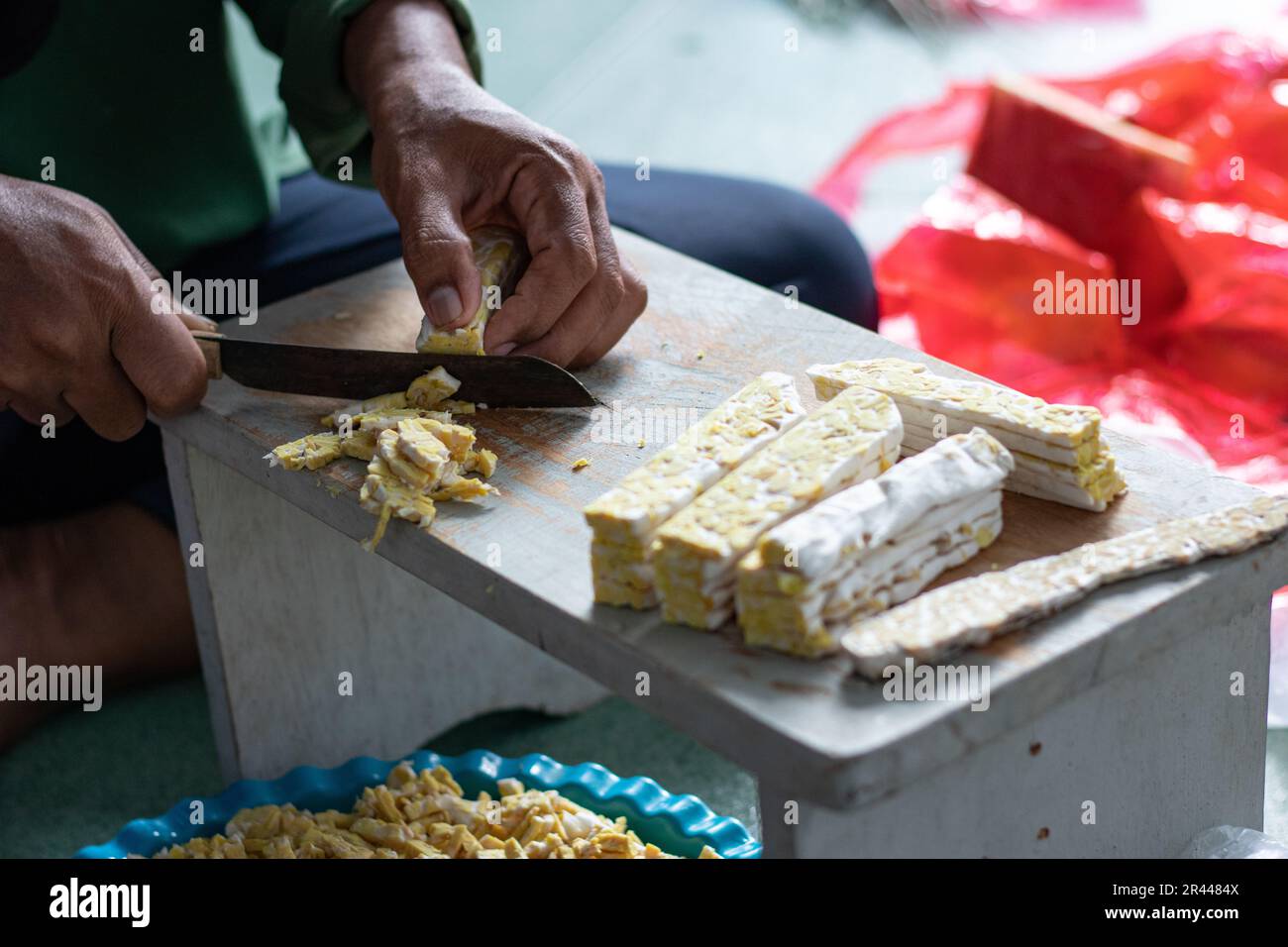 Femme asiatique tranchant le tempeh cru sur la table en bois à l'aide d'un couteau. Le tempeh ou tempe est un produit de soja fermenté originaire d'Indonésie Banque D'Images