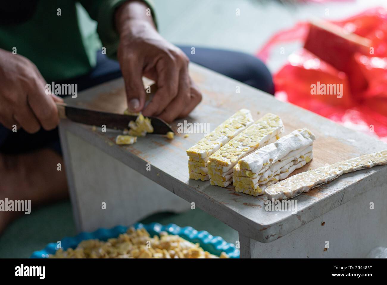 Femme asiatique tranchant le tempeh cru sur la table en bois à l'aide d'un couteau. Le tempeh ou tempe est un produit de soja fermenté originaire d'Indonésie Banque D'Images