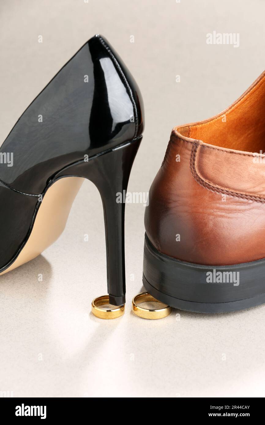 Le talon de la femme et la chaussure de l'homme sont entrés sur des anneaux de mariage dorés sur fond gris clair. Concept de divorce Banque D'Images