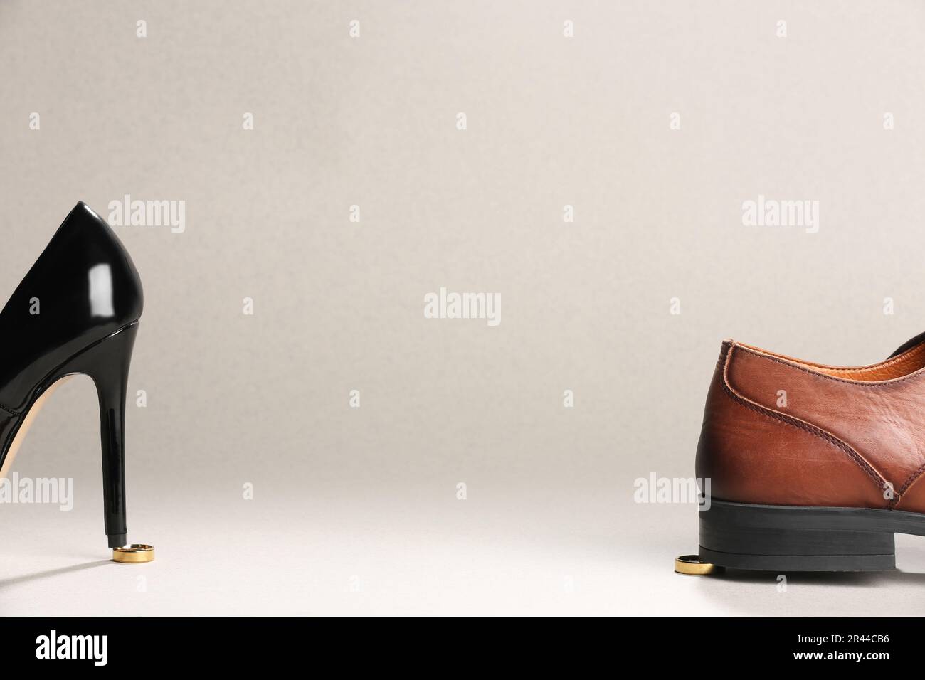 Le talon de la femme et la chaussure de l'homme sont étagés sur des anneaux de mariage dorés sur fond blanc, espace pour le texte. Concept de divorce Banque D'Images