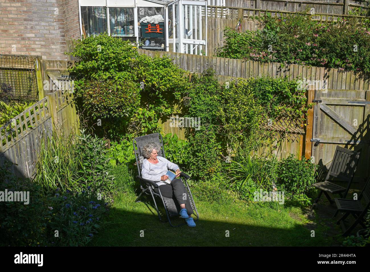 Femme qui se bronzer dans un petit jardin urbain lisant un livre à Brighton UK pendant le soleil de printemps Banque D'Images