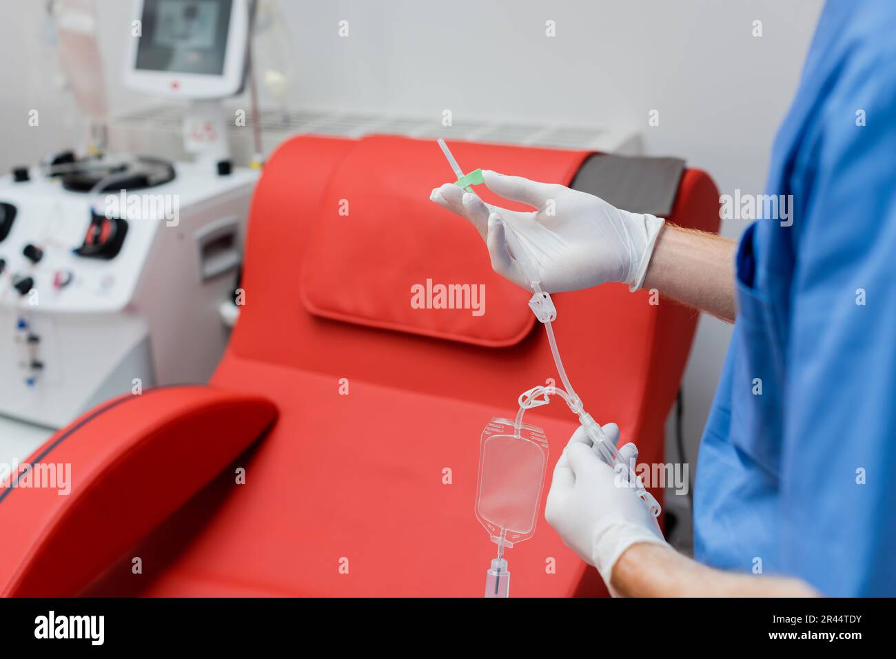 vue partielle d'un praticien dans des gants stériles en latex tenant le kit de transfusion sanguine près d'une chaise médicale avec un design ergonomique confortable et une qu moderne Banque D'Images