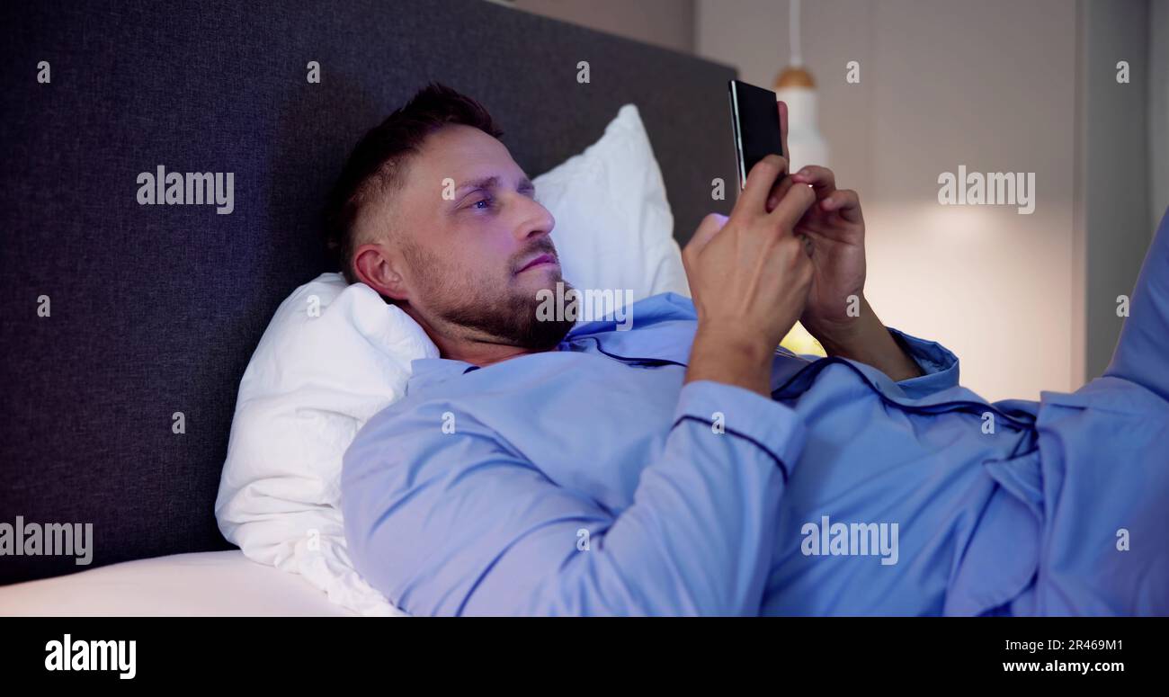 L'homme au lit avec un téléphone mobile dans la nuit Banque D'Images