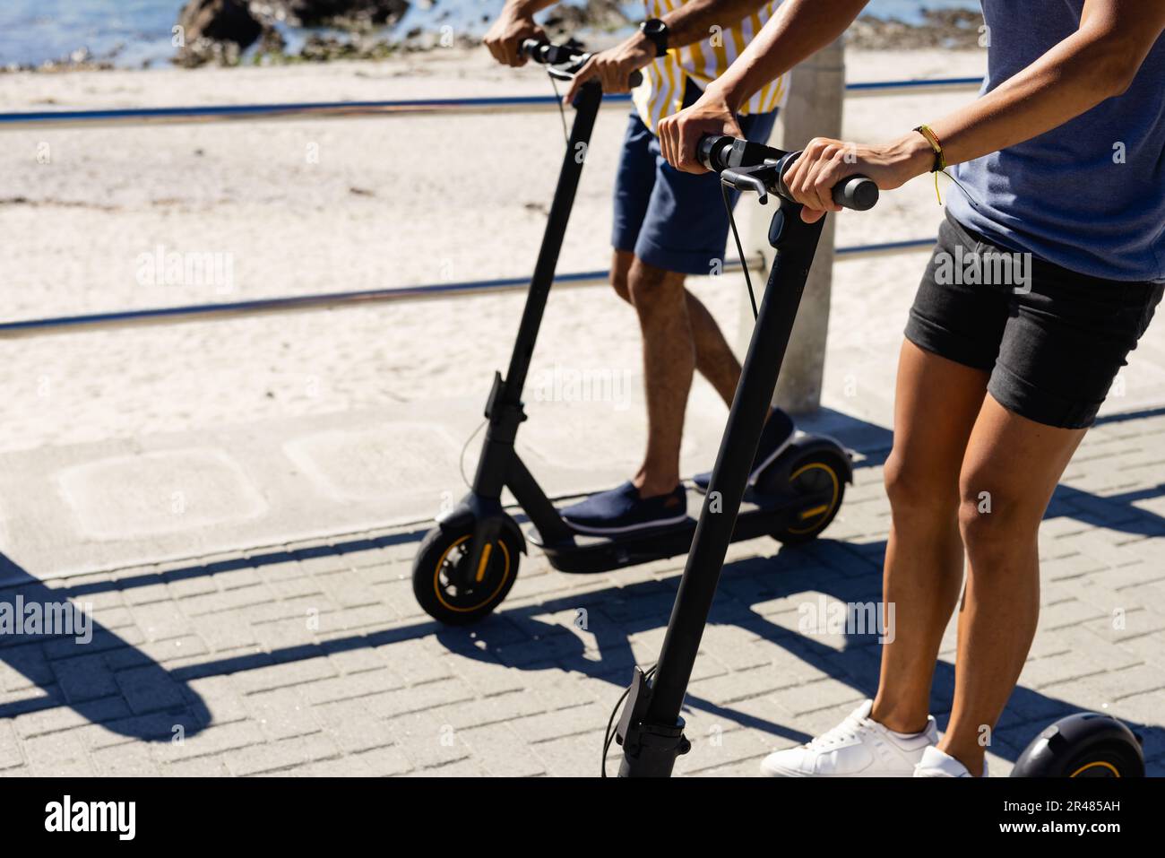 Section médiane de couple de sexe masculin gay biracial à cheval en scooter sur la promenade au bord de la mer Banque D'Images