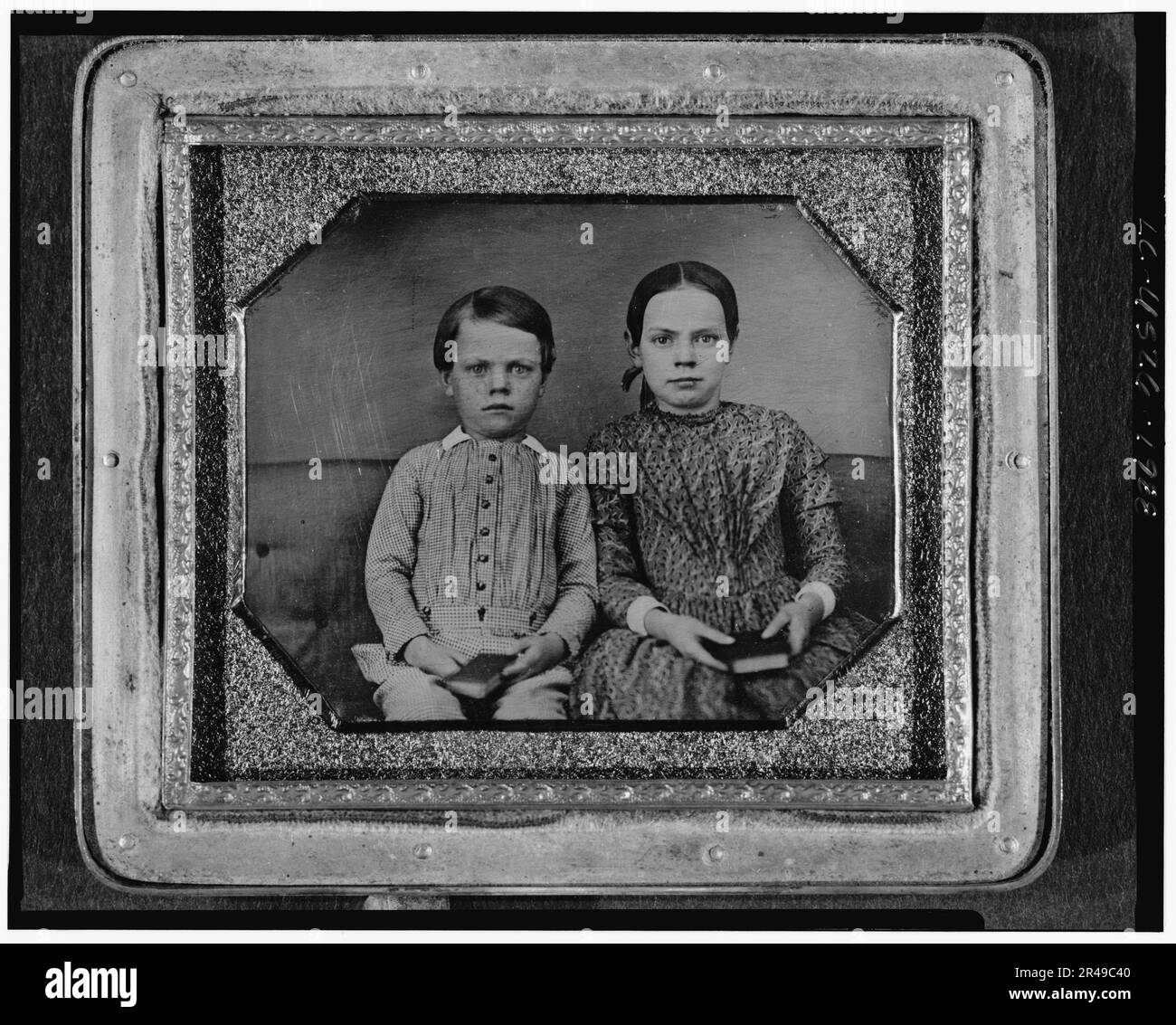 Portrait de groupe d'un garçon et d'une fille non identifiés, trois quarts de longueur, assis sur un banc rembourré, face à l'avant, tenant des livres, entre 1840 et 1860. Banque D'Images