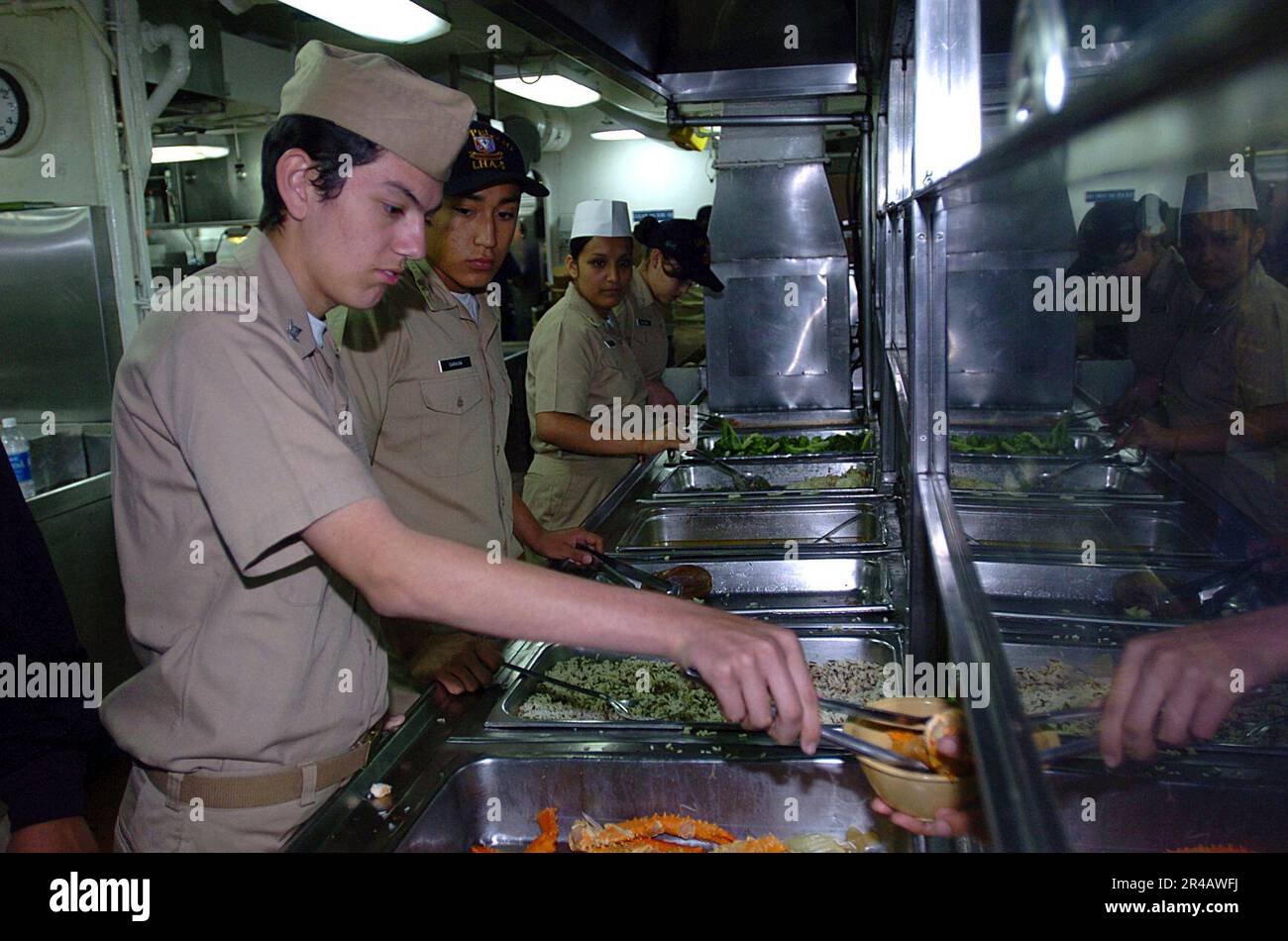 US Navy Junior Reserve Officers Training corps (NJROTC) la classe Petty Officer 3rd sert des pattes de crabe dans les lignes de mess aux marins à bord du navire d'assaut amphibie USS Peliu (LHA 5). Banque D'Images