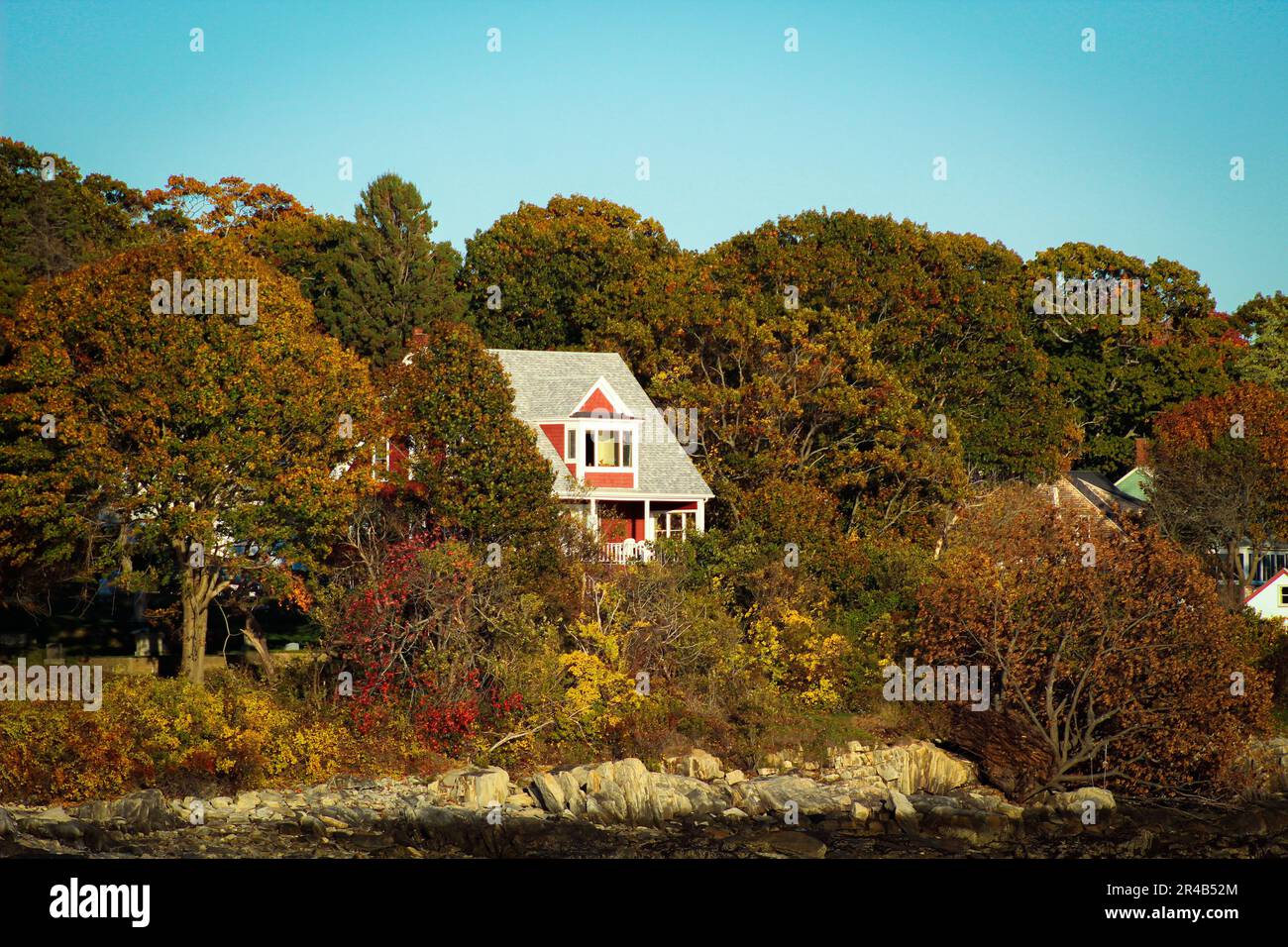 Une luxueuse maison rouge de deux étages avec une pelouse bien entretenue située près d'un plan d'eau avec de grands arbres et des arbustes luxuriants en arrière-plan Banque D'Images