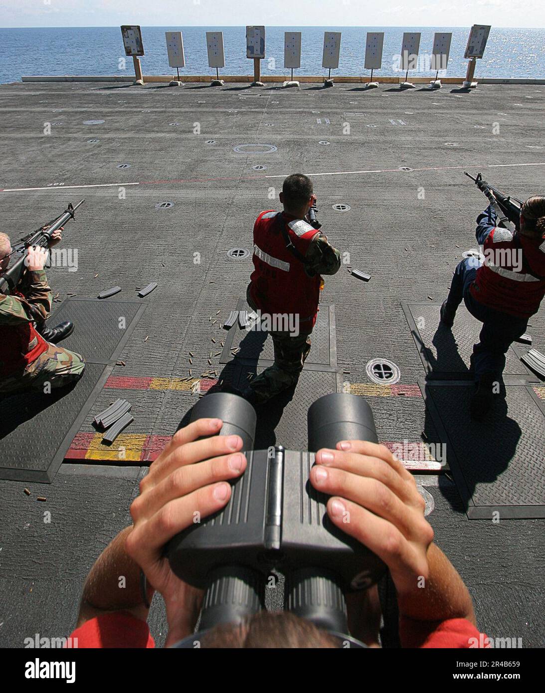 US Navy Un observateur de sécurité de ligne de tir vérifie la précision de la cible tandis que les marins tirent des mitrailleuses M-16 de la position de genou pendant une qualification de armes légères à bord du porte-avions USS de la classe Nimitz. Banque D'Images