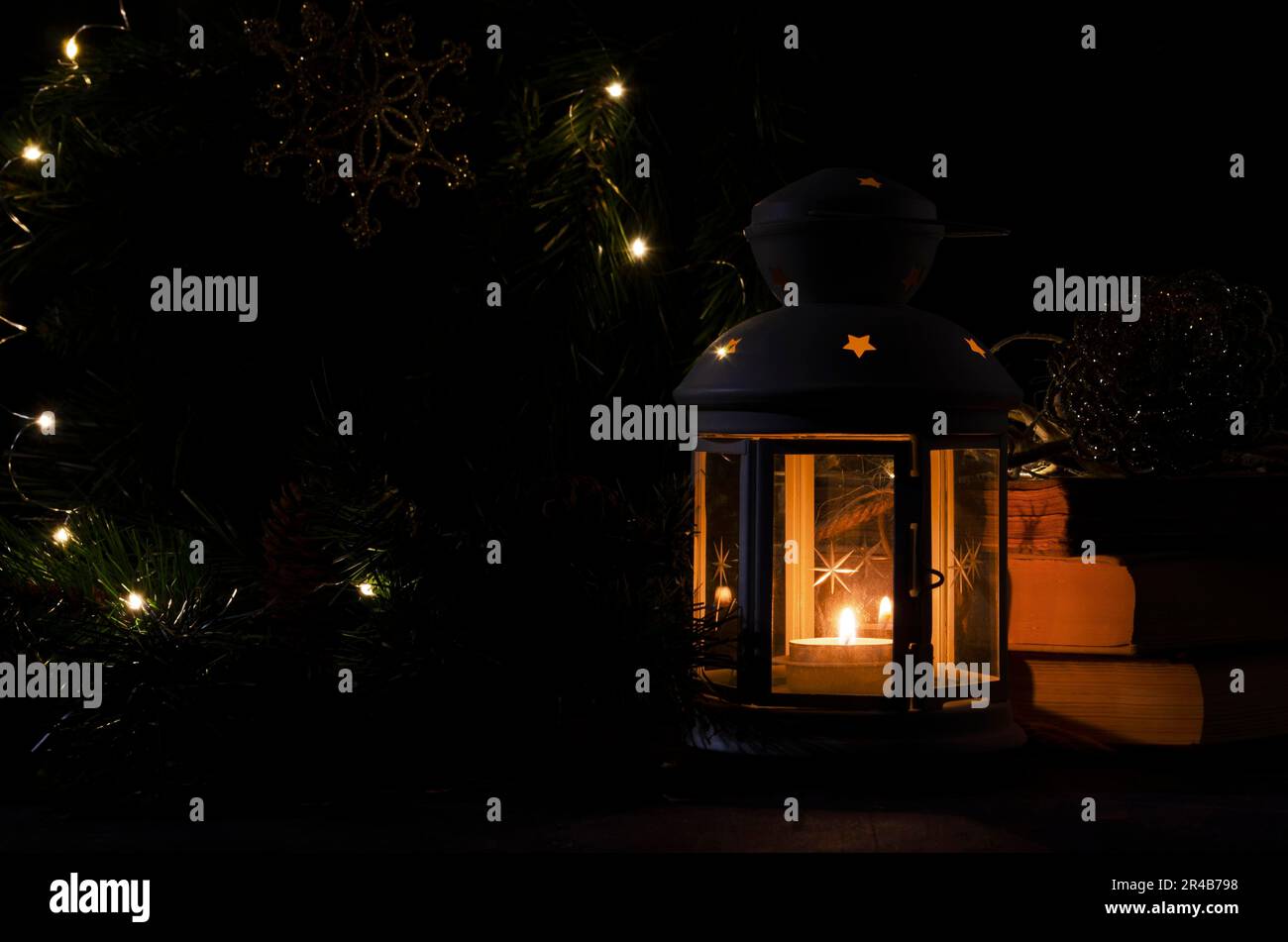 Lanterne blanche avec une bougie allumée. Livres, branche d'arbre de noël et lumières sur fond. Image sombre de nuit. Humeur mystère de Noël Banque D'Images