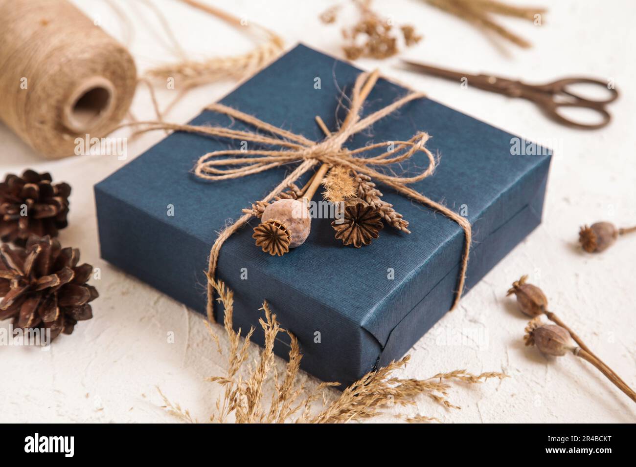 Boîte cadeau faite à la main dans un emballage bleu foncé, têtes de graines de pavot, fleurs séchées sur un bureau blanc. Cadeau pour homme. Fleuriste, herbier artisanal. Couleurs naturelles. Banque D'Images