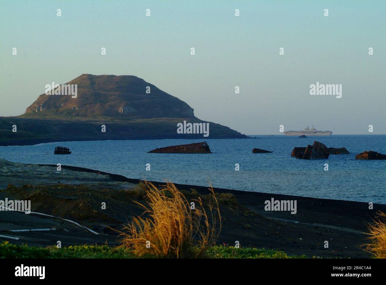 US Navy le navire d'assaut amphibie USS Essex (LHD 2) navigue dans les eaux au large de l'île d'Iwo Jima avec Mt. Suribachi à proximité. Banque D'Images