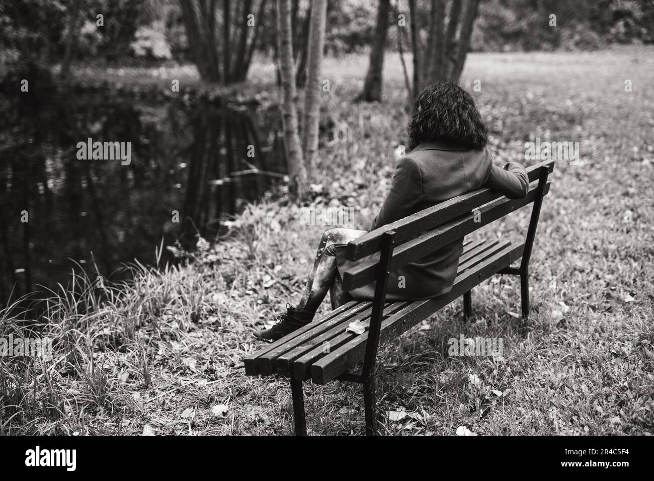 Photographie artistique en noir et blanc d'une jeune femme assise seule sur un banc de parc, son regard est éloigné et réfléchissant Banque D'Images