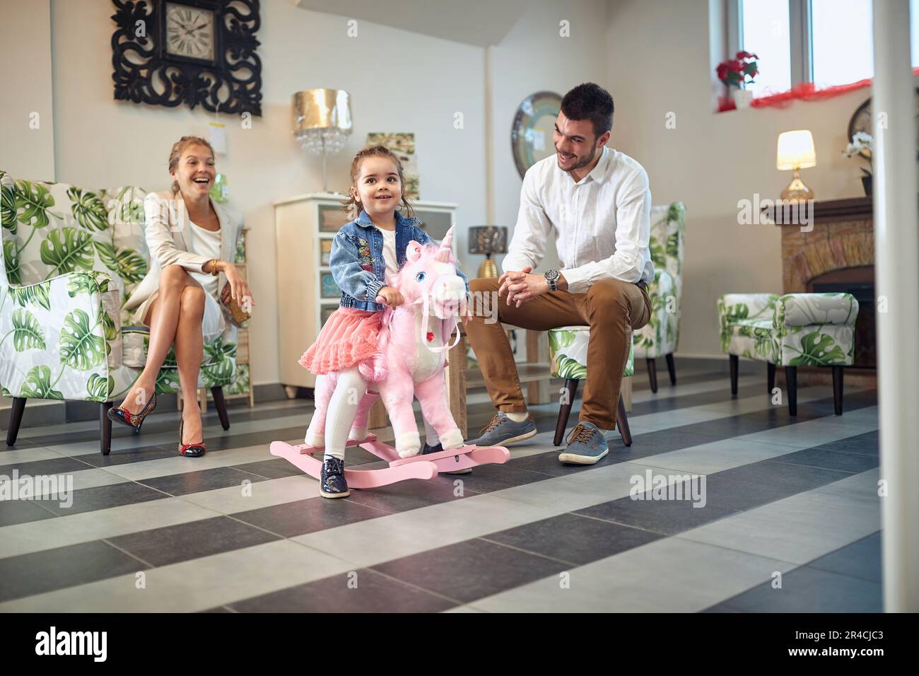 Belle famille de jeune couple et petite fille dans un magasin de meubles moderne, fille sur un cheval de bascule licorne. Shopping, concept de style de vie. Banque D'Images