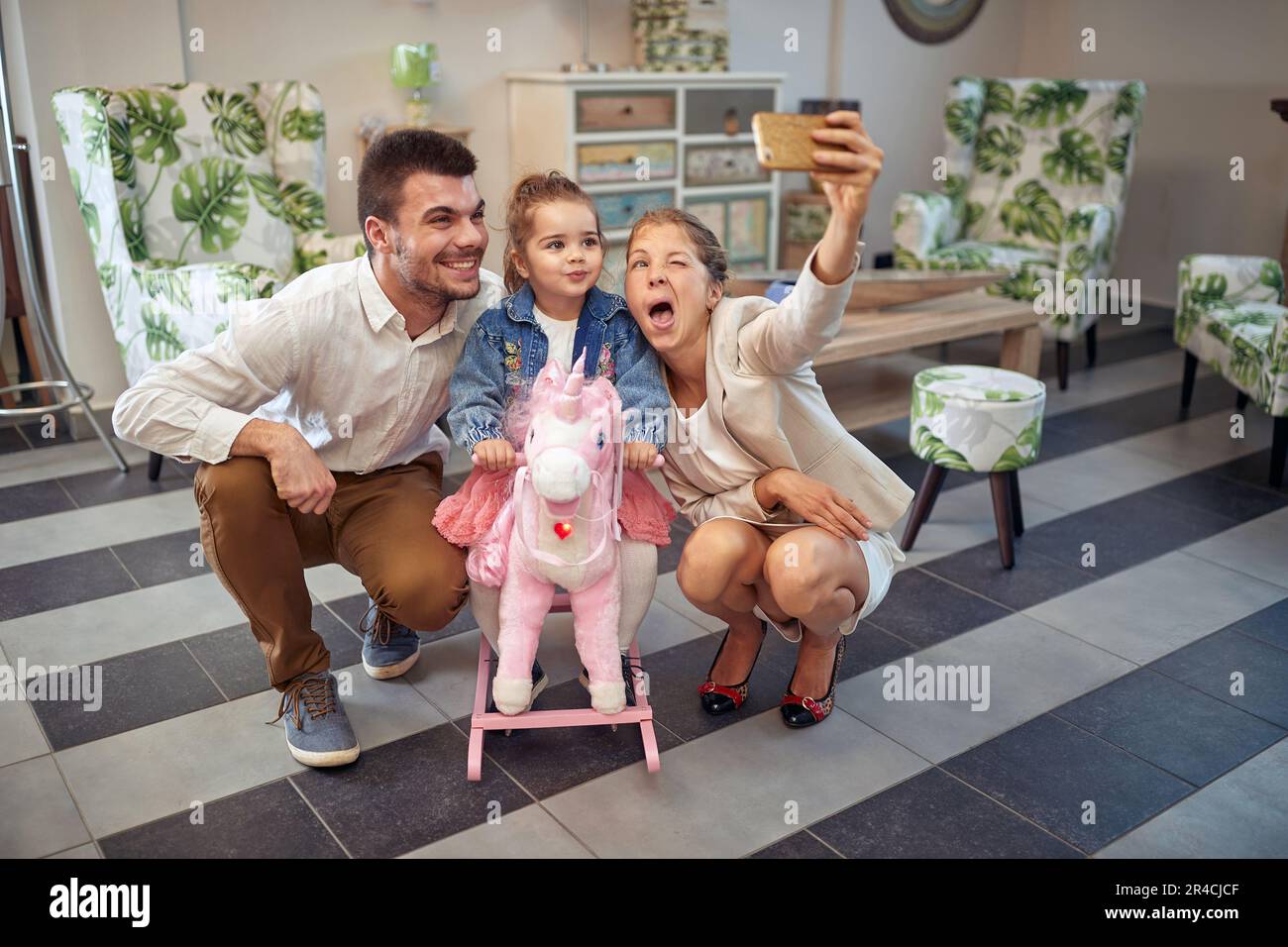 Une famille heureuse dans une boutique de meubles, prenant un selfie, achetant un cheval de bascule unicorn pour petite fille. Famille, style de vie, concept de shopping. Banque D'Images