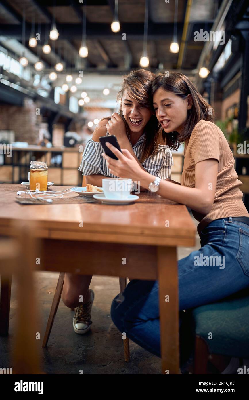 Deux jeunes filles belles dans le café ayant un grand moment. Femme montrant quelque chose sur son téléphone à sa petite amie. Concept de divertissement, de convivialité et de style de vie. Banque D'Images