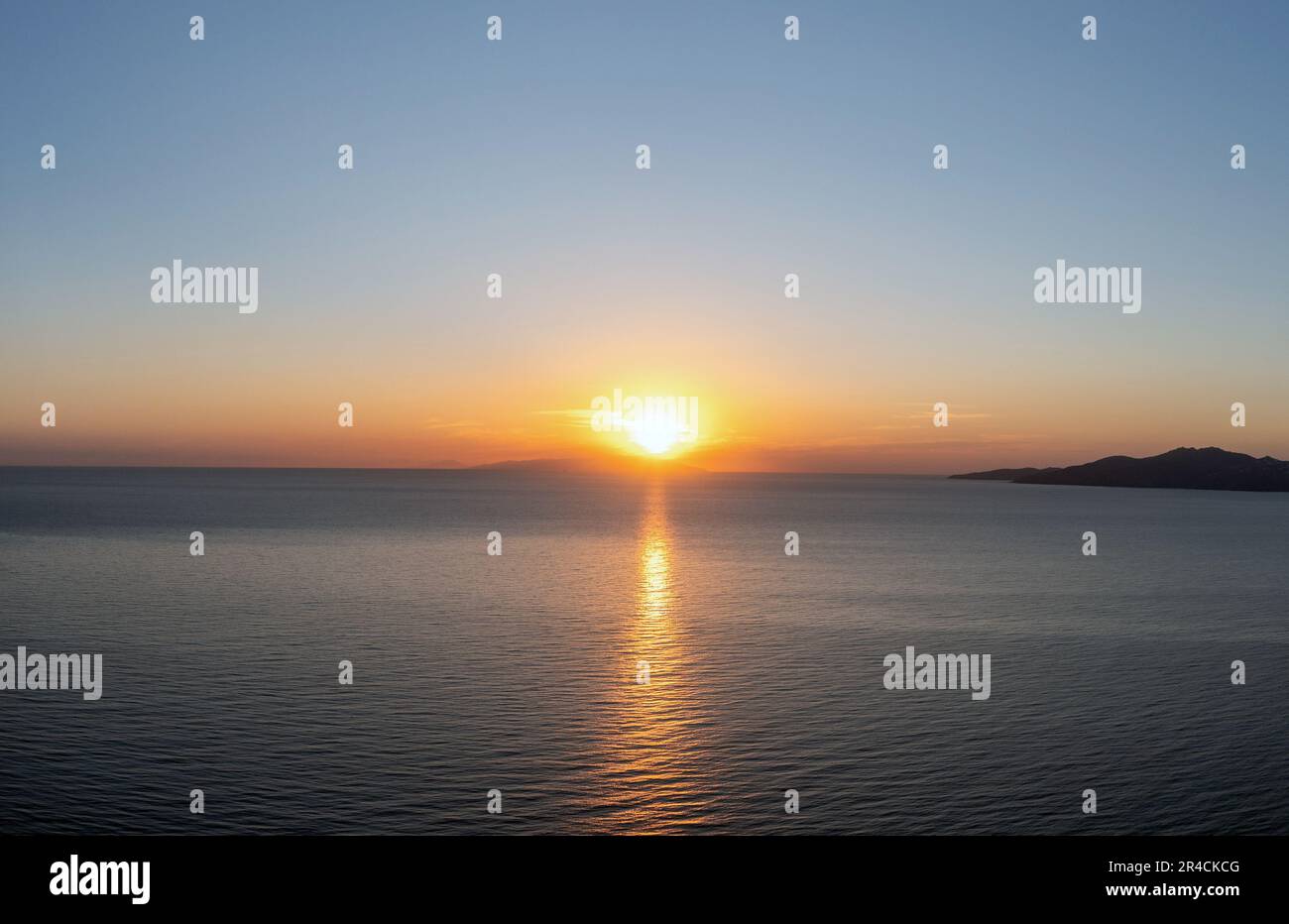 Coucher de soleil sur l'île grecque, Cyclades, Grèce. Le soleil doré se cache derrière la colline au coucher du soleil et colore l'or vaste mer bleu Egée calme. Banque D'Images