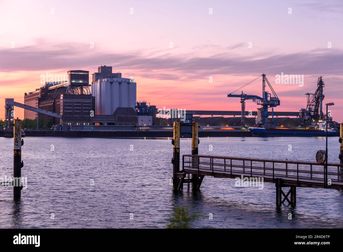 Quai commercial avec silos et vieilles serres de guerre sur un port fluvial au crépuscule Banque D'Images