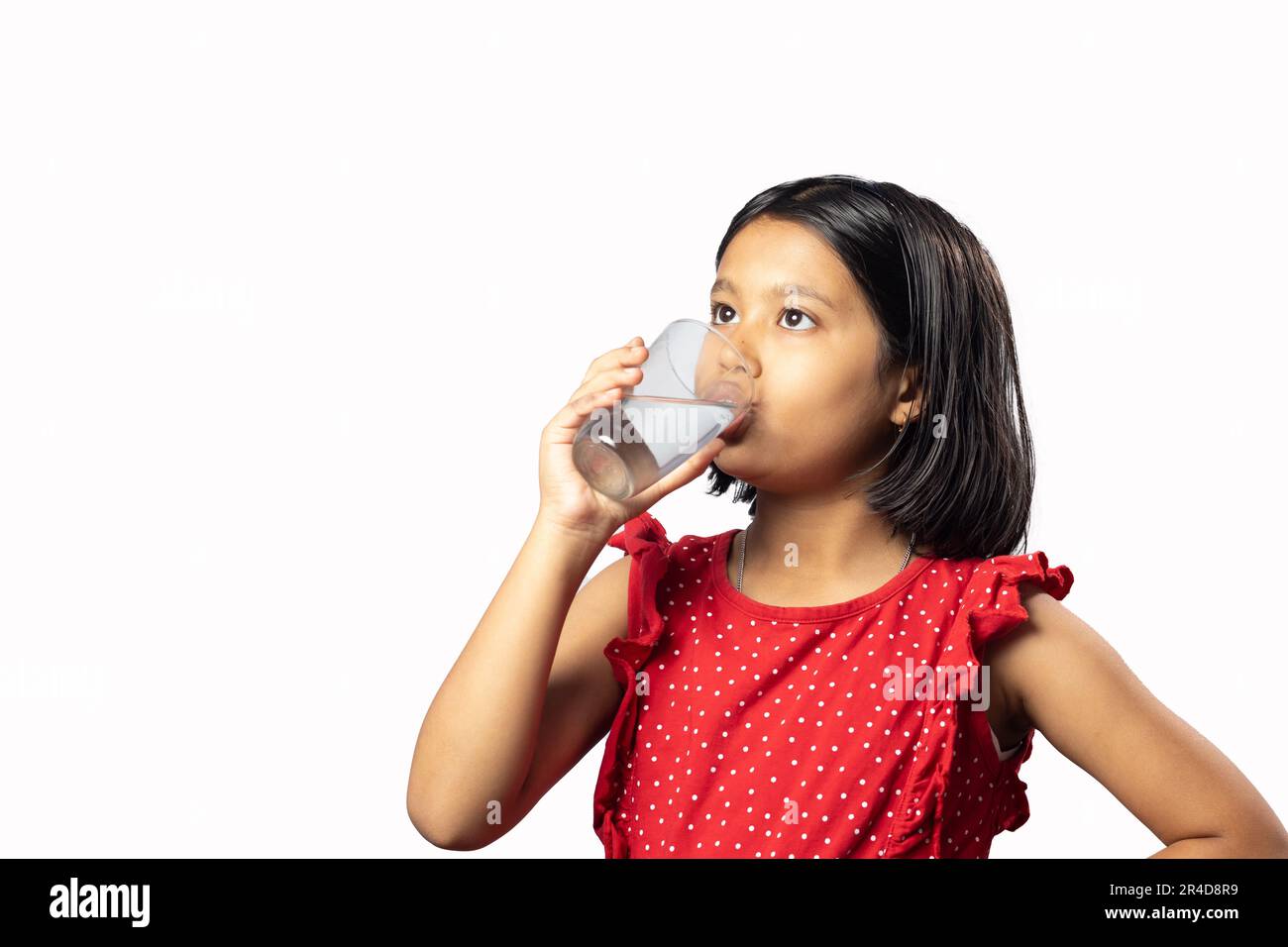 Une fille asiatique indienne en robe rouge boire de l'eau à partir d'un verre sur fond blanc Banque D'Images