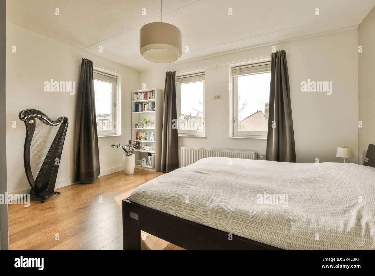 une chambre avec parquet et draps blancs sur le lit, il y a une grande harpe noire dans le coin de la chambre Banque D'Images