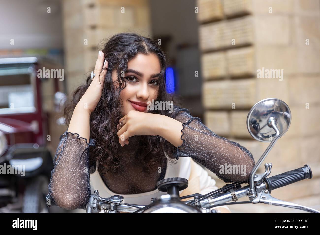 Portrait de sexy tannées fille assise sur une moto vintage avec la main dans ses cheveux. Horizontalement. Banque D'Images