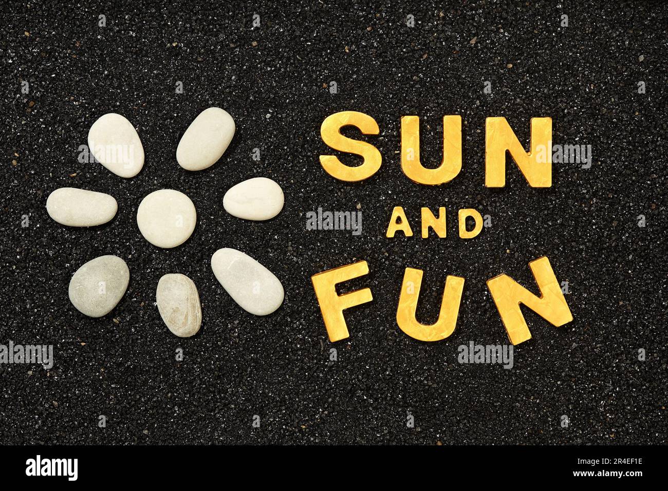 Soleil et plaisir - texte dans le sable noir de plage avec le symbole du soleil par les galets de mer Banque D'Images
