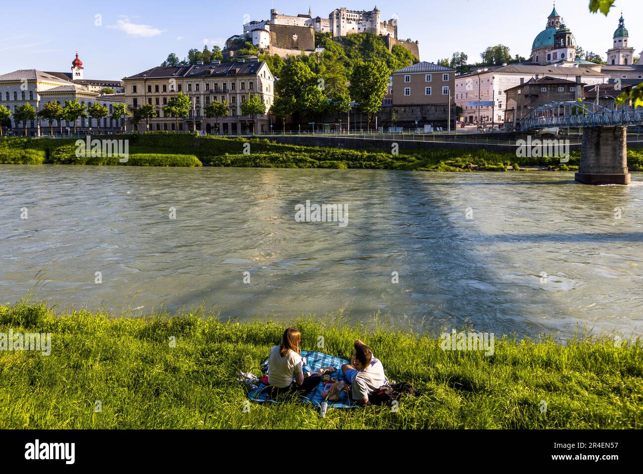 Les rives de la rivière Salzach avec vue sur la forteresse de Hohensalzburg et le quai de la cathédrale sont un lieu de pique-nique populaire pour les couples à Salzbourg, en Autriche Banque D'Images