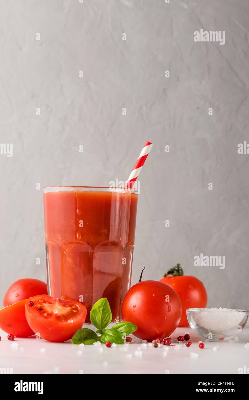 Jus de tomate dans un verre avec paille et tomates fraîches, basilic, sel et poivre sur table en marbre blanc Banque D'Images