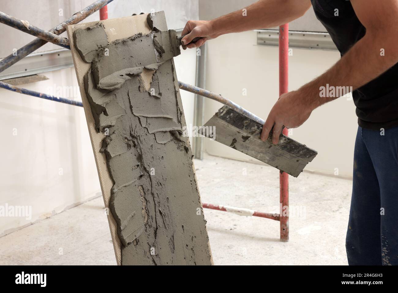L'employé répandant le mélange d'adhésif sur les carreaux avec une spatule, gros plan Banque D'Images