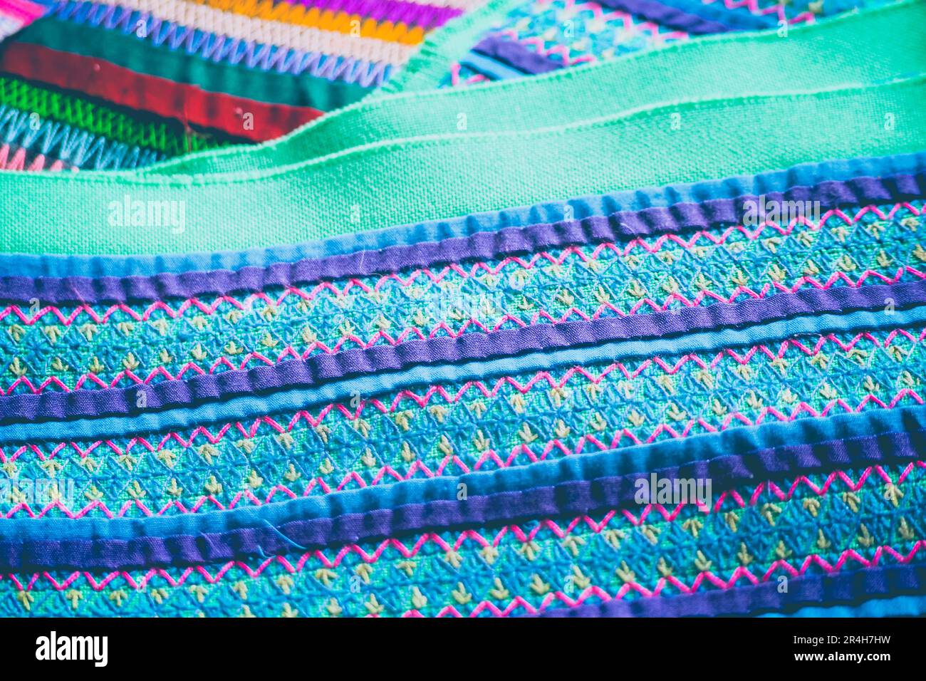 Vue macro détaillée de broderies tribales éclatantes avec coutures géométriques complexes et fils turquoise violet et vert vif Banque D'Images