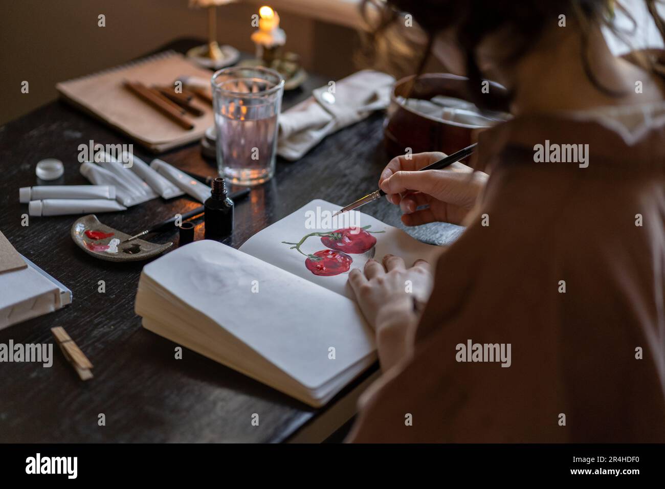 Femme artiste assise à table avec bougies en feu de peinture dans le carnet de croquis Banque D'Images