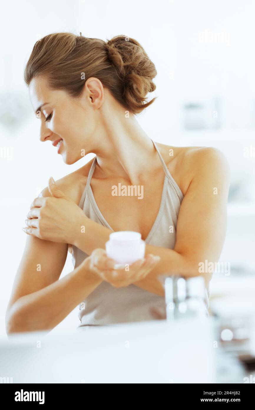 Happy young woman applying cream dans salle de bains Banque D'Images