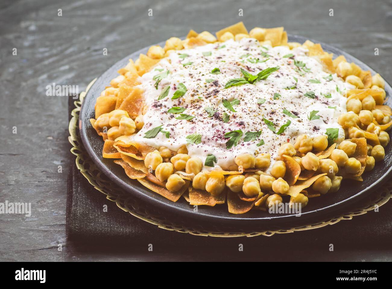 Cuisine arabe ; authentique libanais « Fattah » ou « Fatteh » avec pain pita grillé, pois chiches et sauce au yaourt sur fond sombre rustique. Banque D'Images