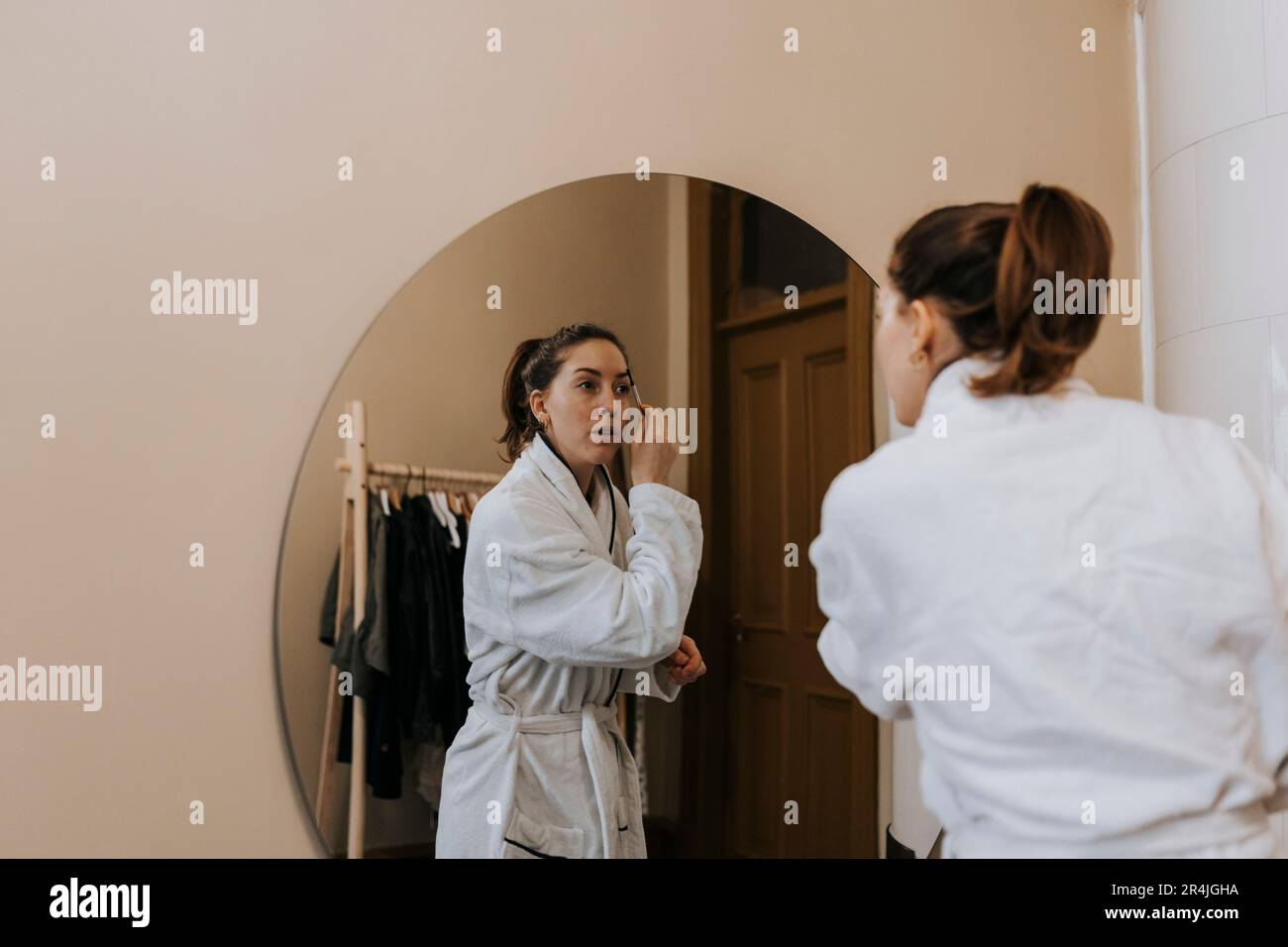 Personne non binaire utilisant un crayon de sourcil tout en regardant dans le miroir à la maison Banque D'Images