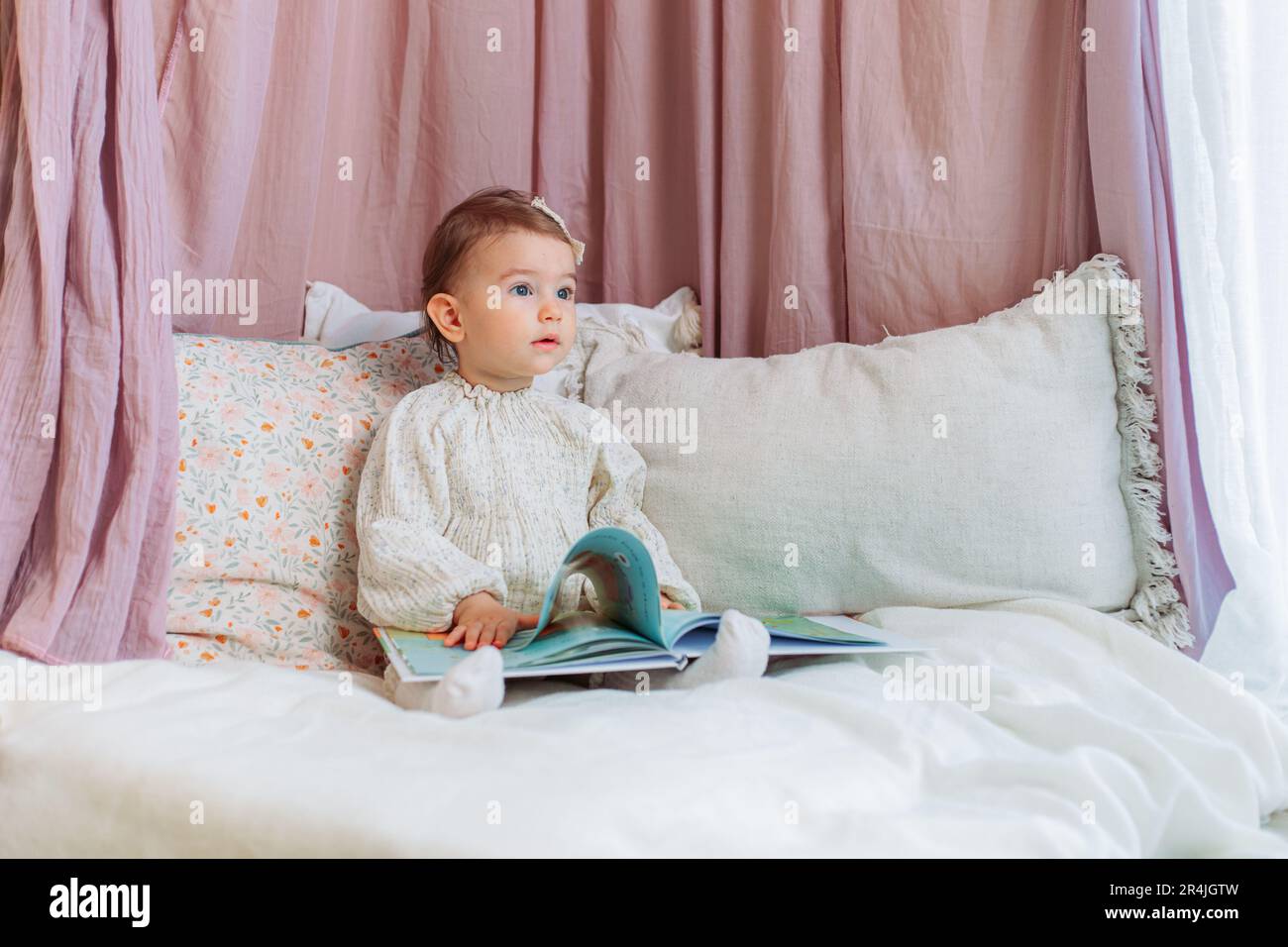 Mignon, petite fille de bébé assis sur les oreillers lisant un livre Banque D'Images