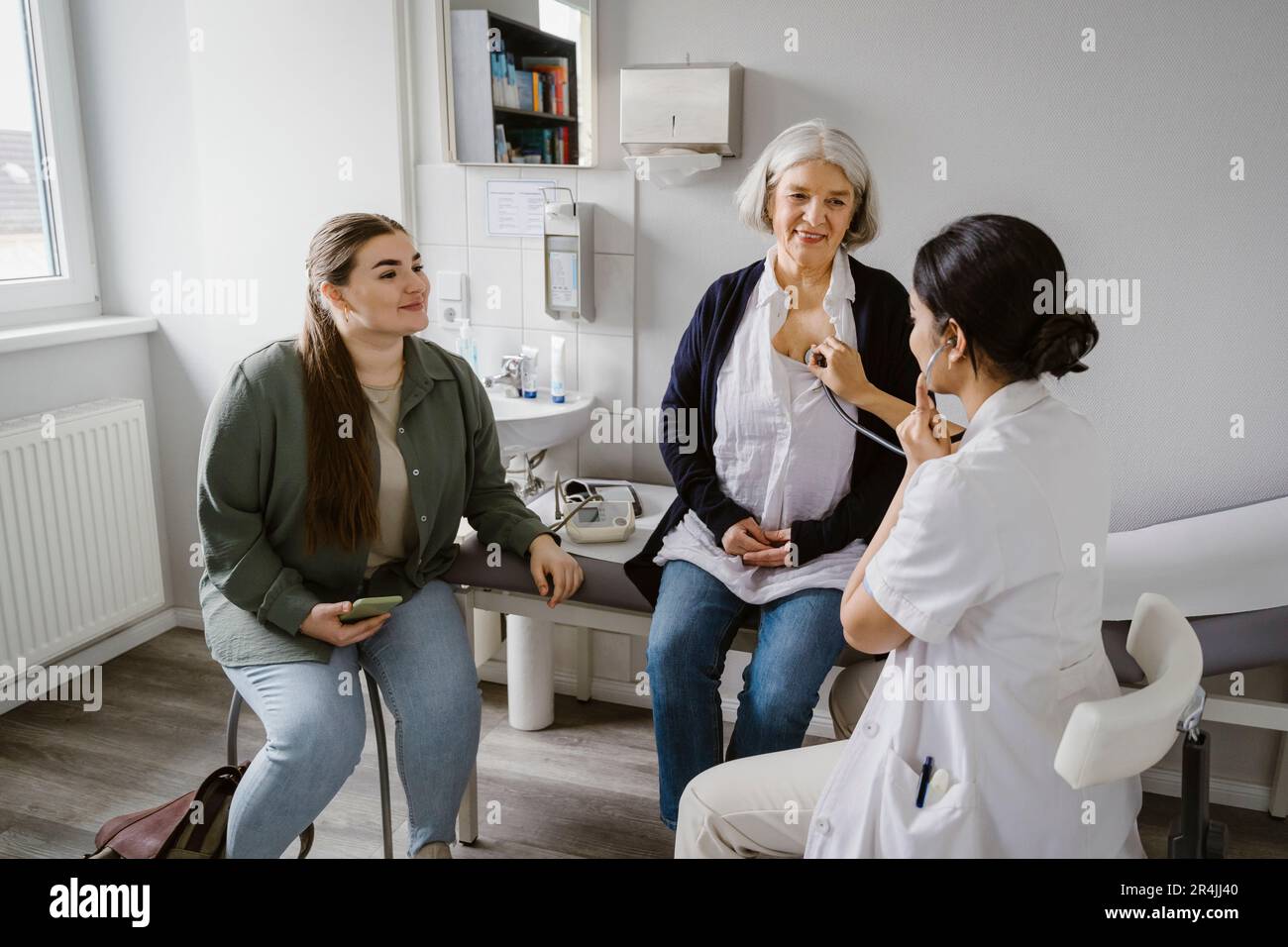 Un médecin écoute le rythme cardiaque d'une femme âgée assise avec sa fille à la clinique Banque D'Images