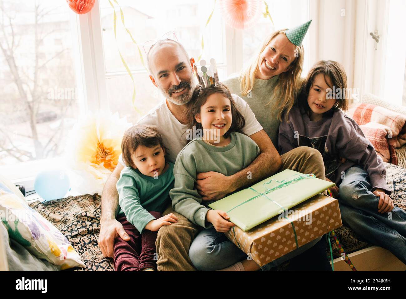 Portrait d'une jeune fille heureuse assise avec des cadeaux et de la famille sur un siège en alcôve à la maison Banque D'Images