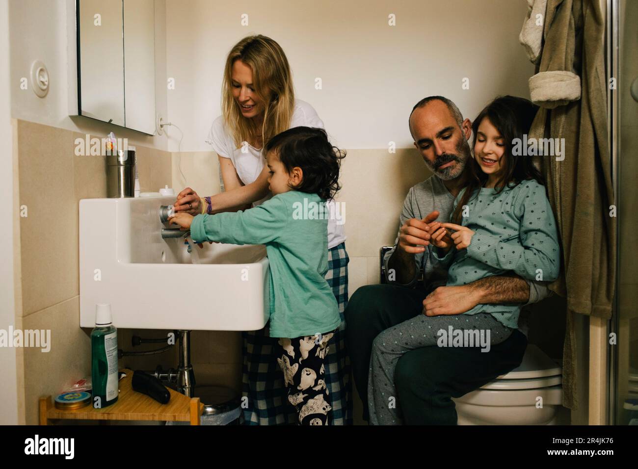 Femme aidant le fils avec se laver les mains tandis que l'homme et la fille parlant dans la salle de bains Banque D'Images