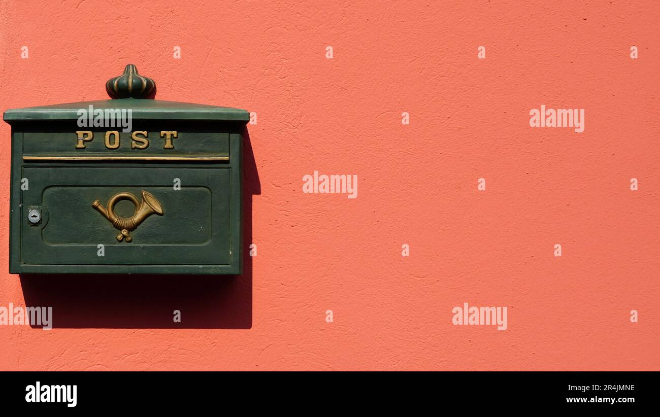Boîte aux lettres en métal vert avec symbole de poteau doré sur mur plâtré orange vif au soleil. Espace pour le texte. Banque D'Images