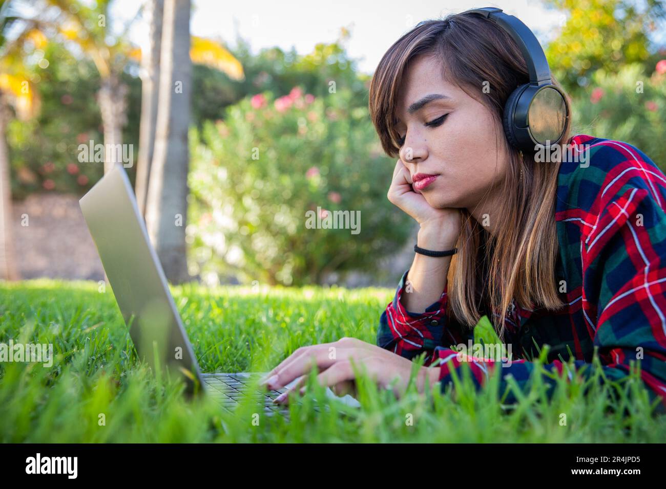 Une jeune femme utilise son ordinateur portable tout en étant allongé sur un pré dans un parc public Banque D'Images