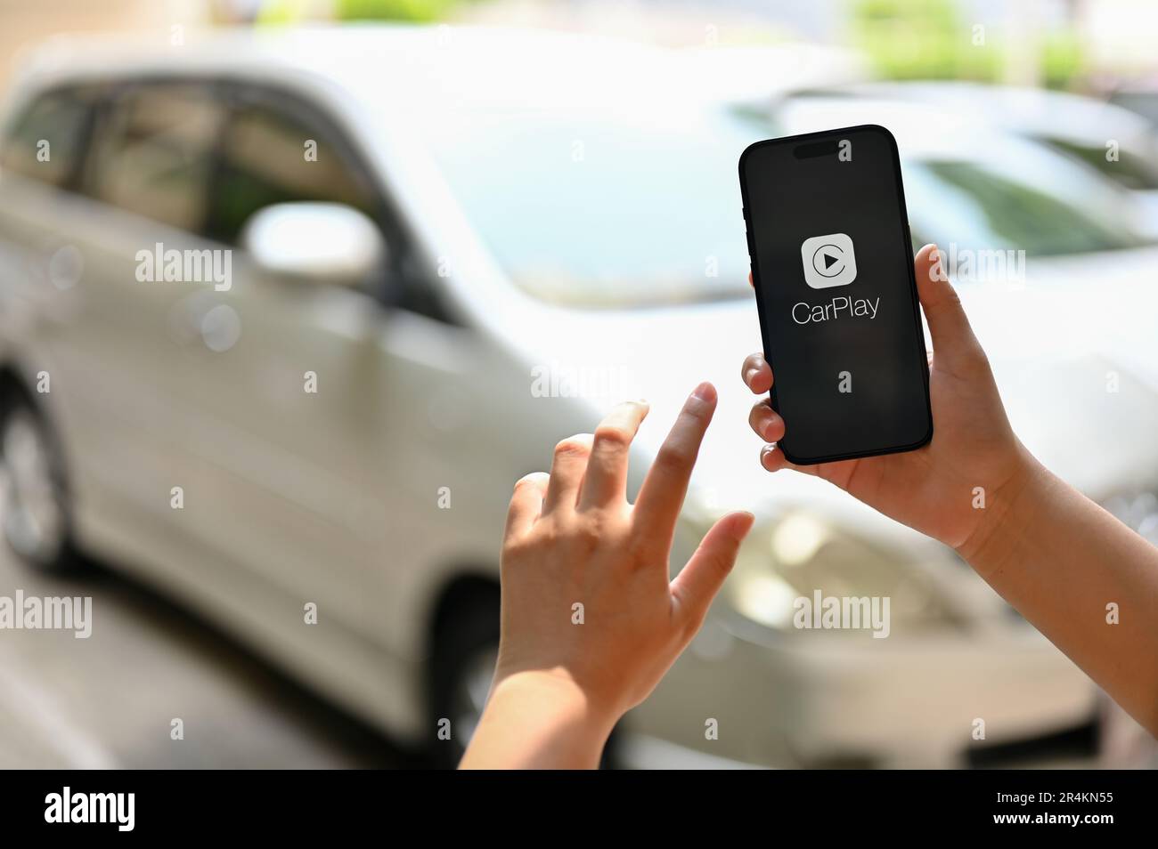 Chiang Mai, Thaïlande - 26 mai 2023: Gros plan d'une main femelle tenant un iPhone avec le logo CarPlay à l'écran sur un arrière-plan flou d'un c Banque D'Images