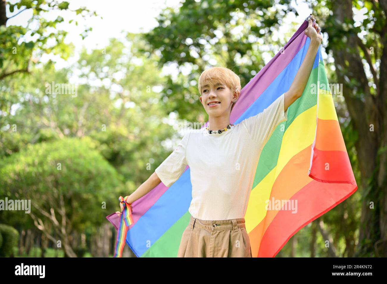 Portrait d'un jeune gay asiatique attrayant et souriant avec un drapeau arc-en-ciel LGBT dans le parc vert, célébrant le mois de la fierté LGBT. Banque D'Images