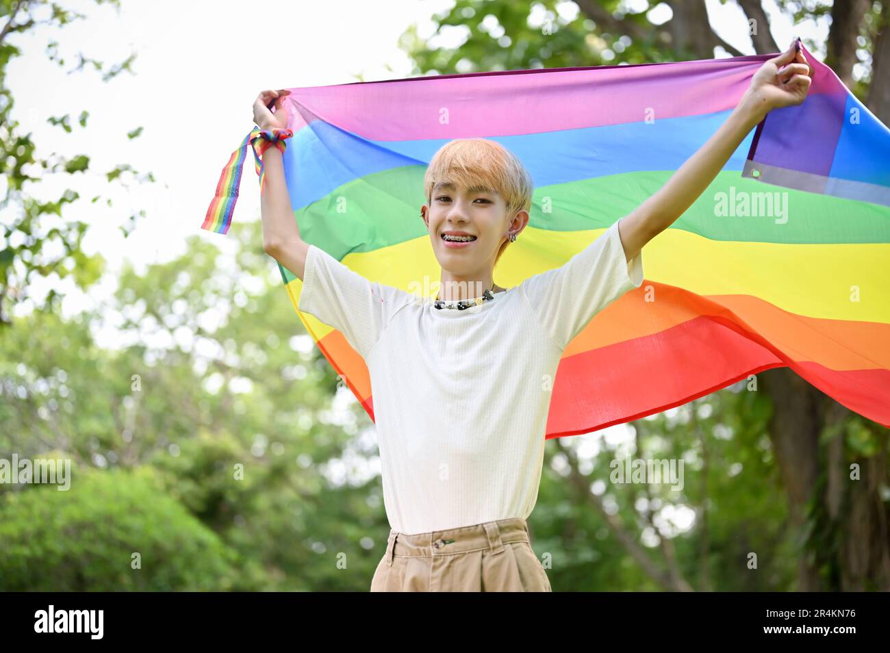 Portrait d'un jeune gay asiatique insouciant et heureux avec un drapeau arc-en-ciel LGBT debout dans le parc vert, célébrant le mois de la fierté. Diversité, humain r Banque D'Images