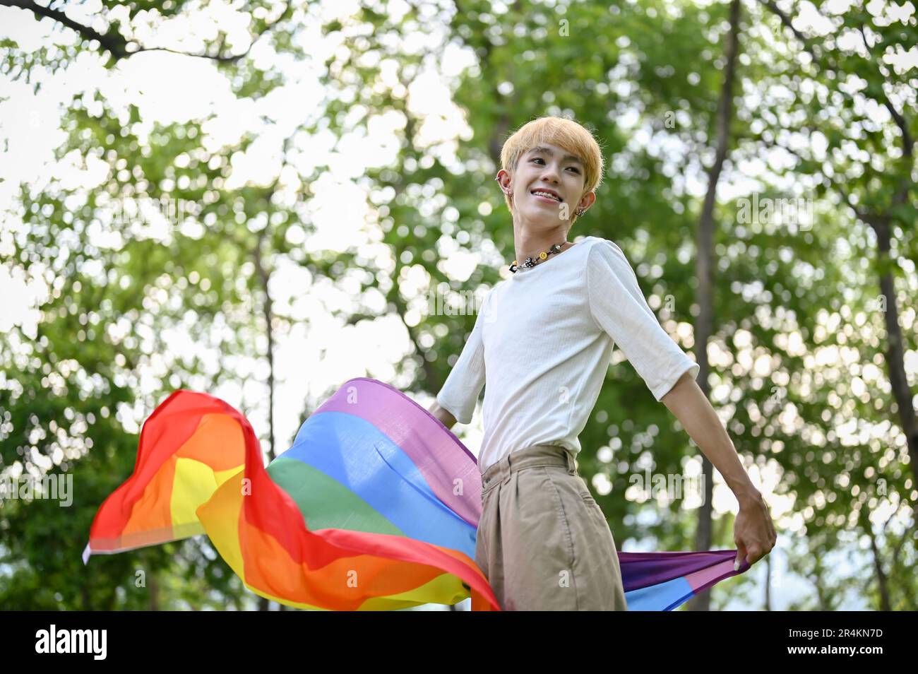 Portrait d'un jeune gay asiatique attrayant et insouciant avec un drapeau arc-en-ciel LGBT debout dans le parc vert. LGBTQ+, Pride Month Banque D'Images