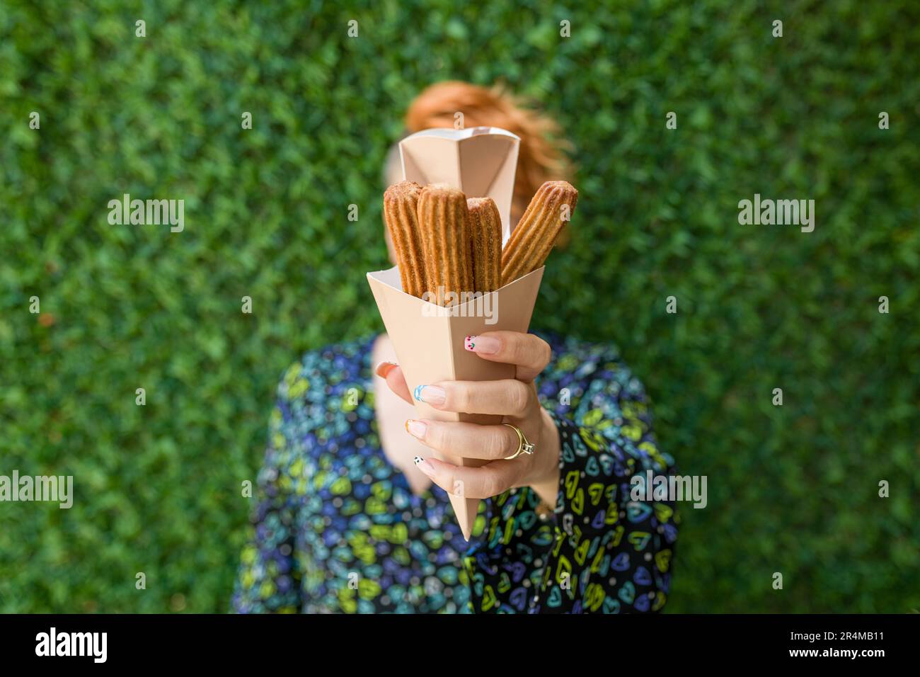 femme tenant des churros dans une boîte en carton devant le mur d'herbe verte Banque D'Images