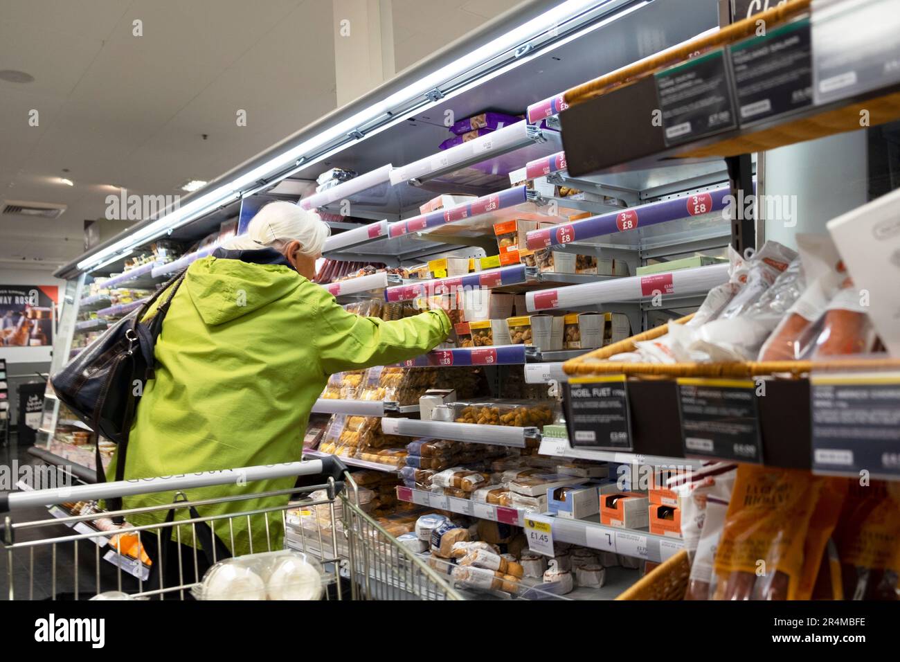 Femme plus âgée avec chariot à provisions regardant la nourriture à vendre sur les étagères de réfrigération dans le magasin Marks and Spencer 2023 Grande-Bretagne KATHY DEWITT Banque D'Images