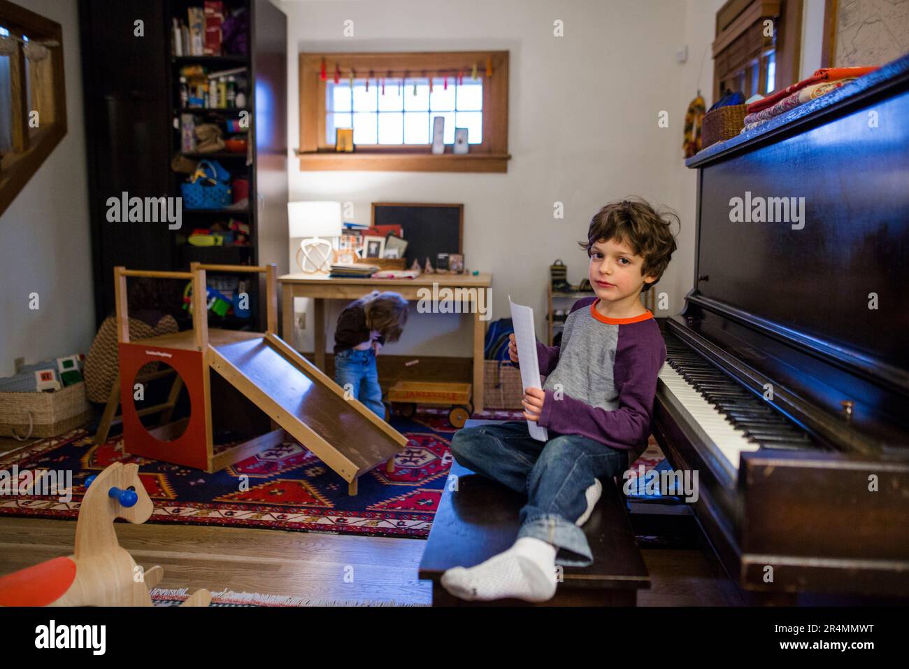 Vue directe d'un petit garçon assis au banc de piano dans son salon Banque D'Images