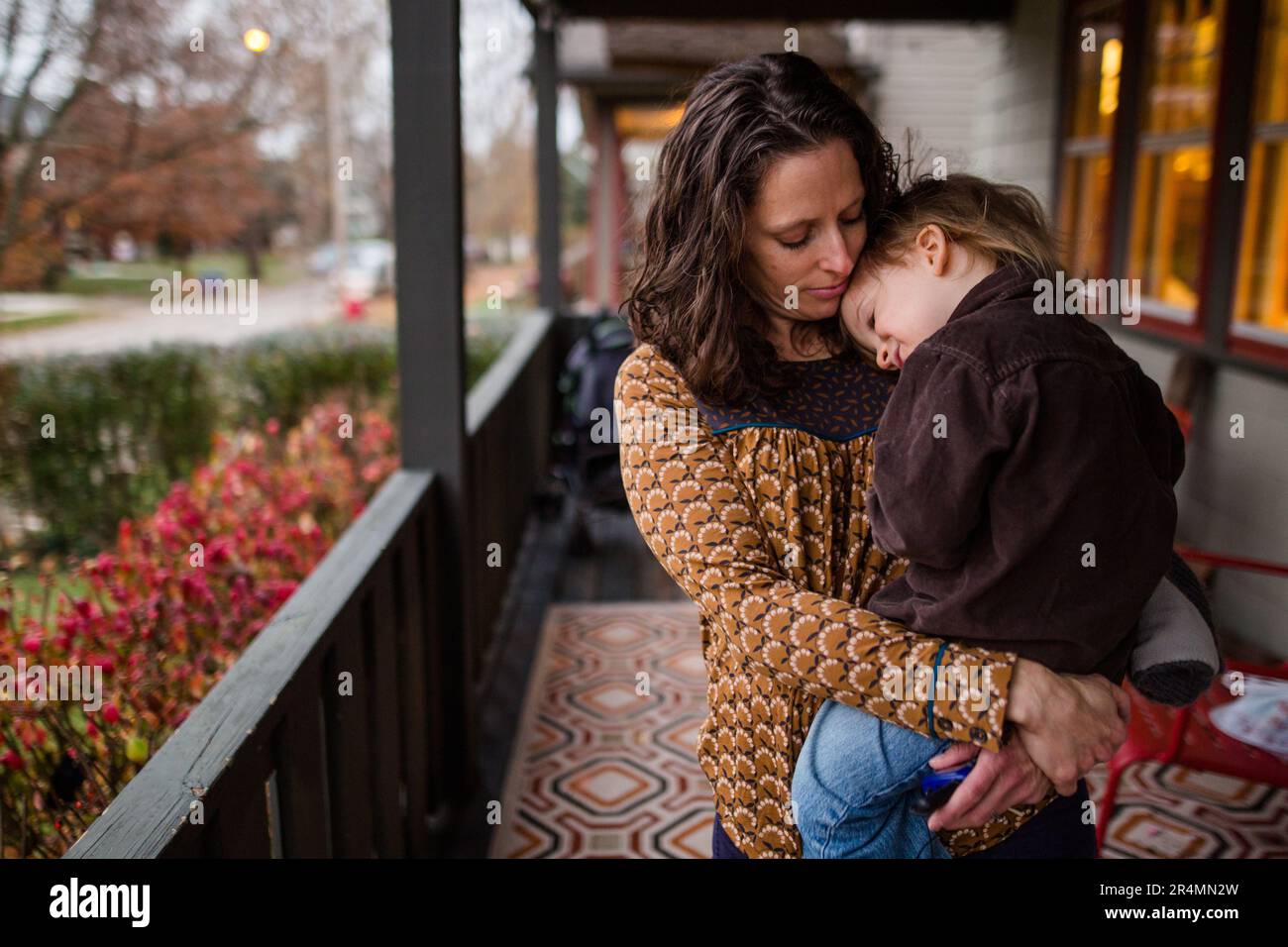 Un petit enfant repose la tête sur l'épaule de sa mère sur le porche au crépuscule Banque D'Images