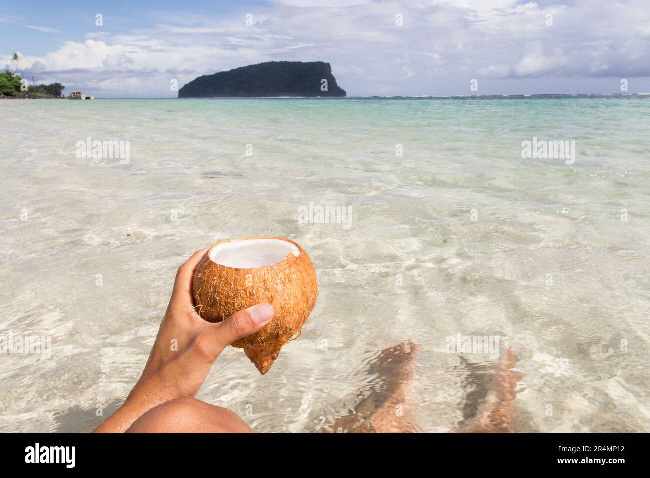 Main tenant la noix de coco fraîche avec des eaux claires comme arrière-plan. Banque D'Images