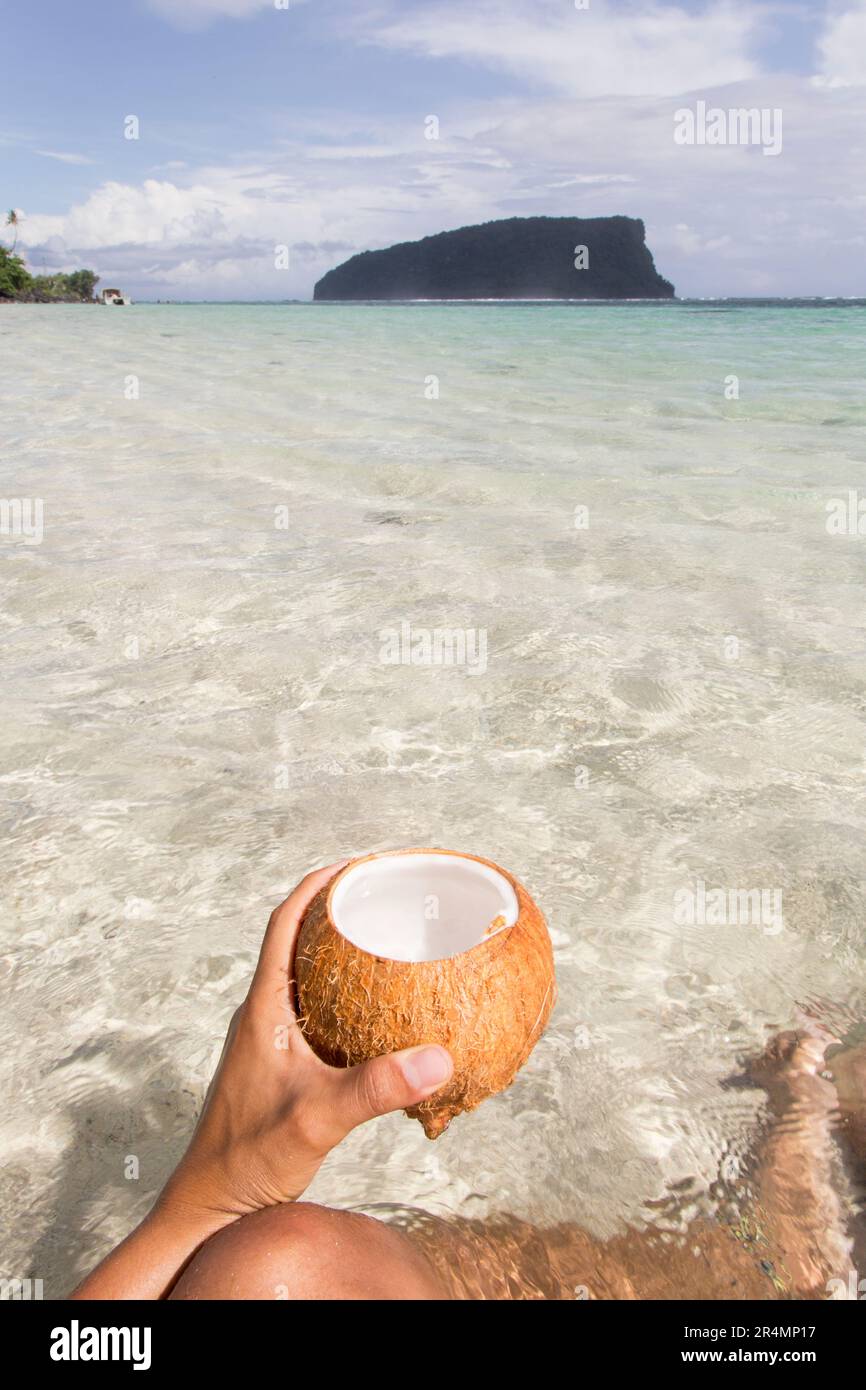 Main tenant une noix de coco avec l'eau turquoise clair comme fond, Samoa Banque D'Images